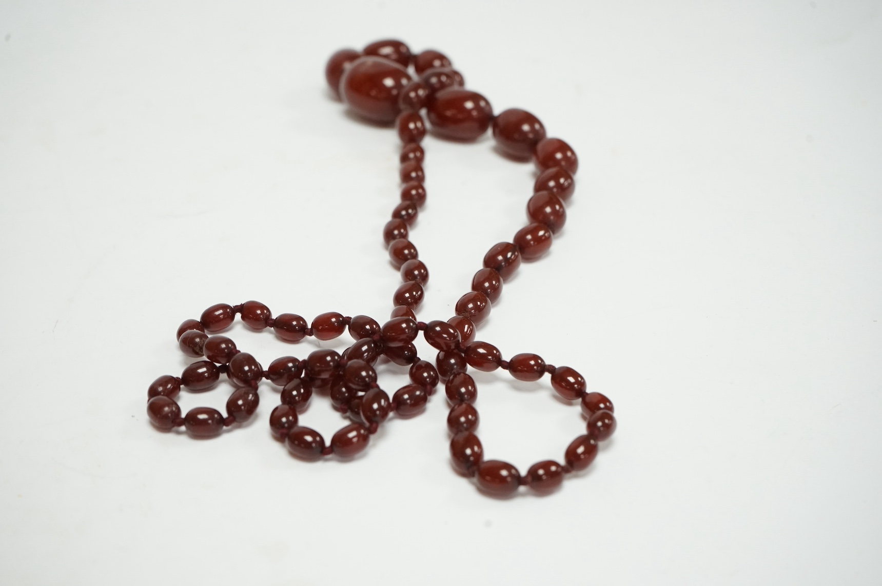 A single strand graduated oval simulated cherry amber bead necklace, 94cm, gross 63 grams. Condition - fair